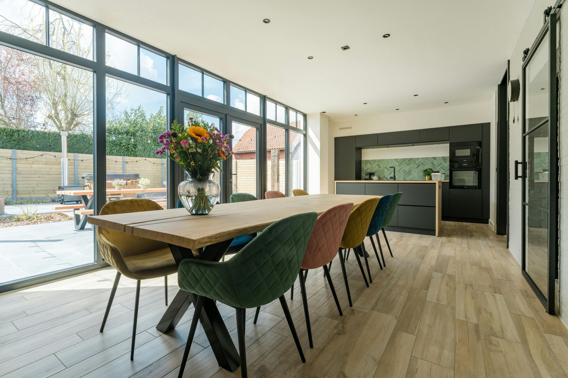 Salle à manger moderne avec de grandes fenêtres et une cuisine en arrière-plan.
