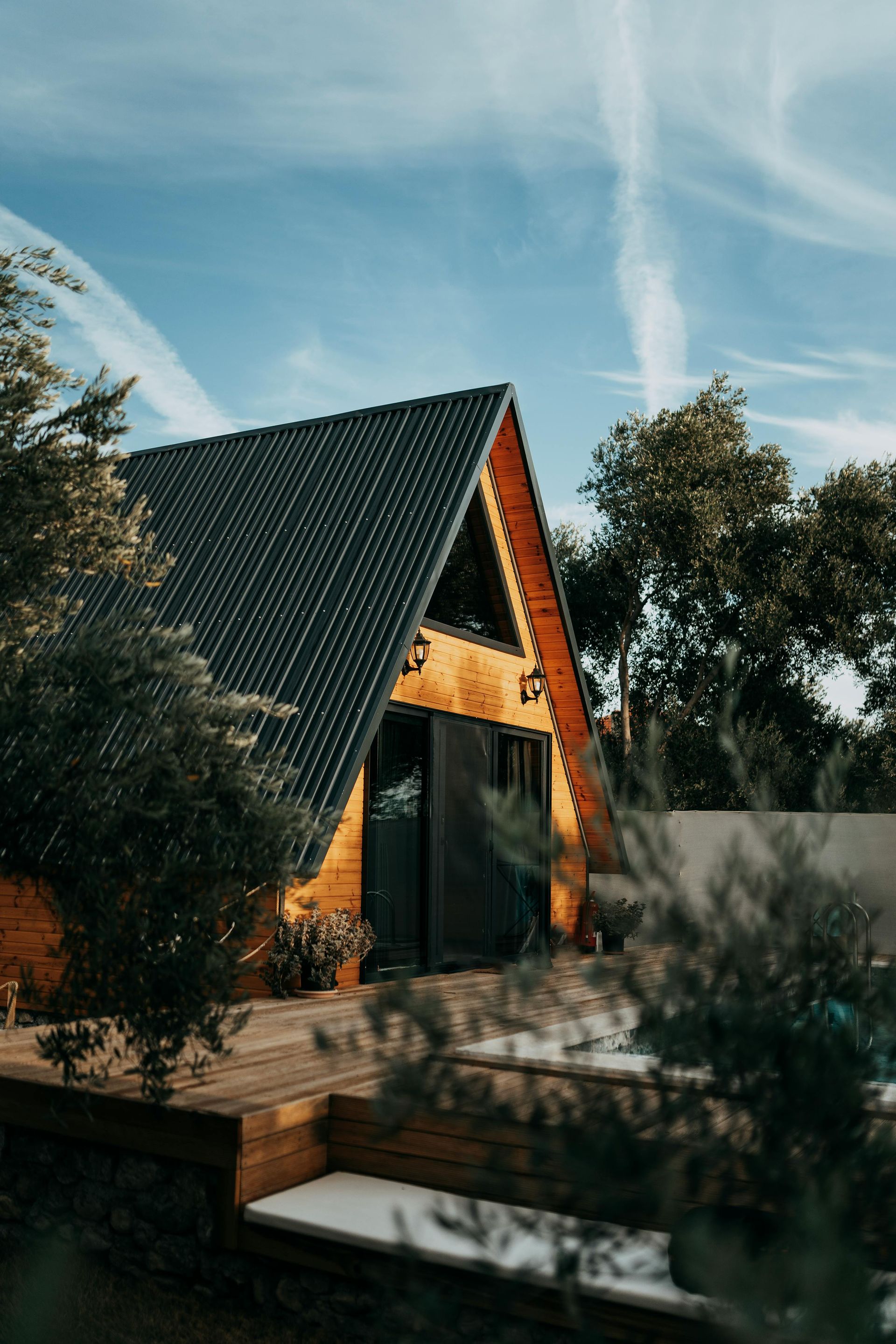 Un chalet moderne en forme de A, au toit noir et aux finitions en bois, entouré d'arbres sous un ciel bleu.