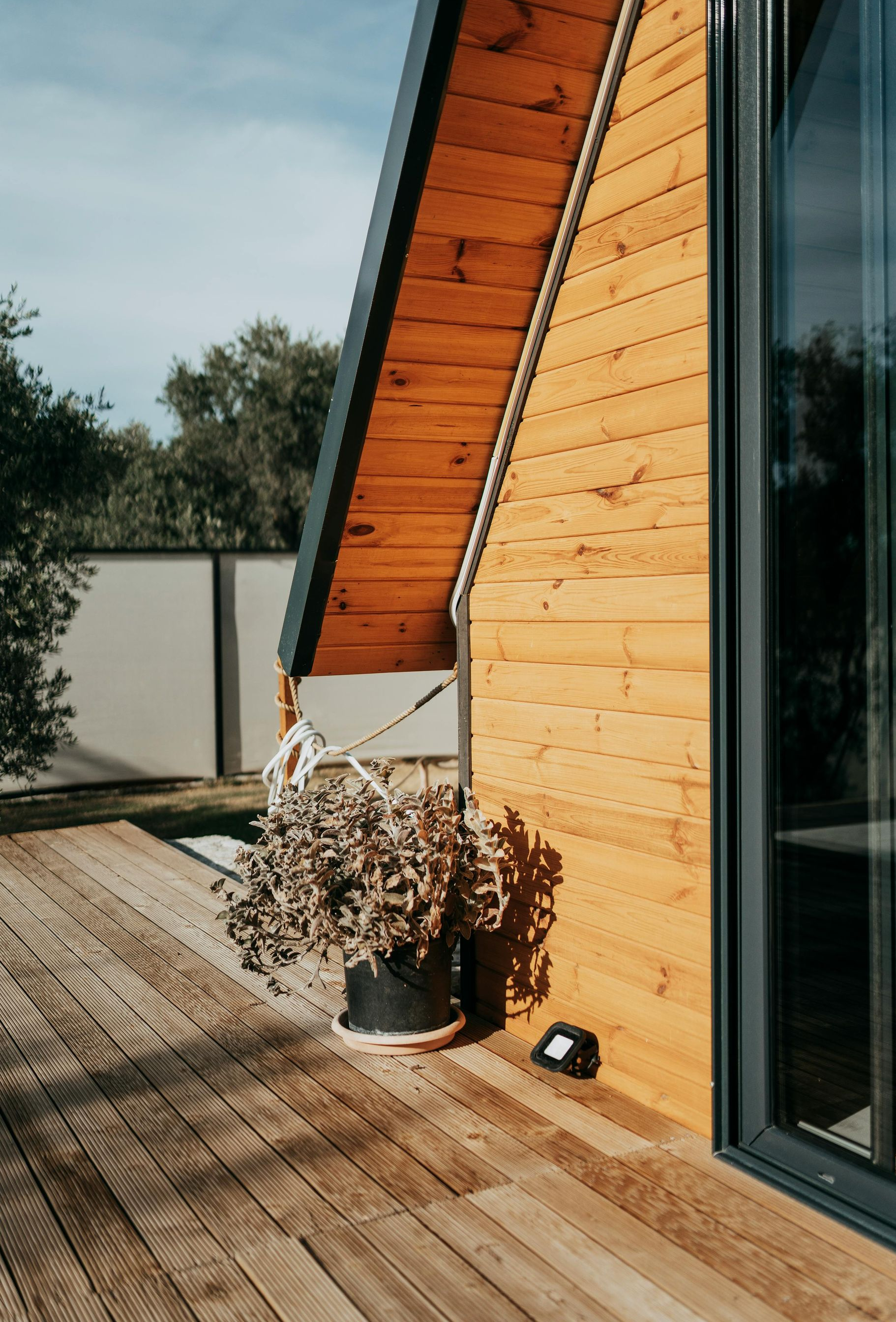 Extérieur d'une maison moderne en bois avec toit en pente, grande porte vitrée et plante en pot sur une terrasse