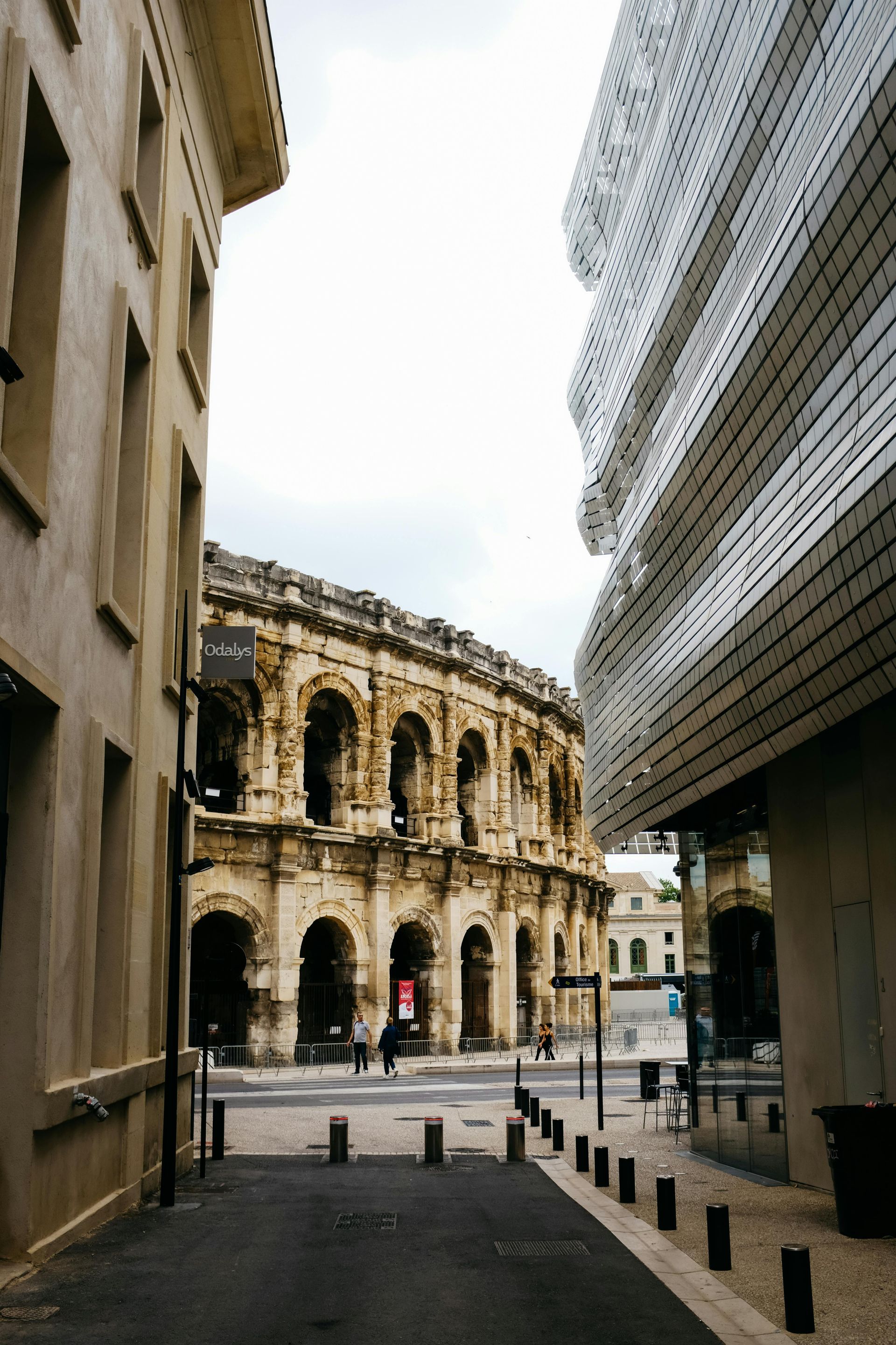 Amphithéâtre historique en pierre, visible entre des bâtiments modernes dans une rue de la ville