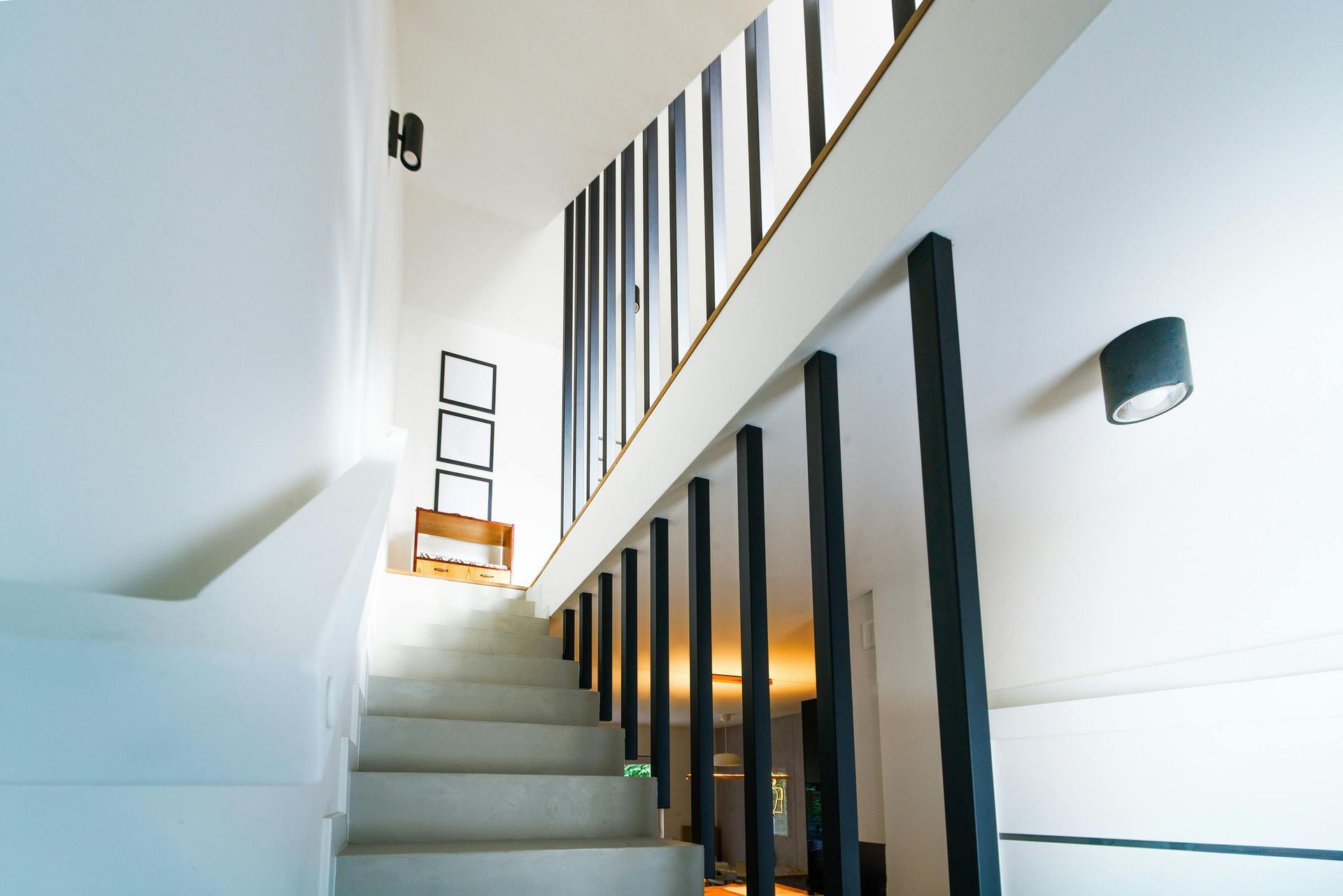 Escalier moderne avec murs blancs, rampe noire et hautes fenêtres dans un intérieur lumineux