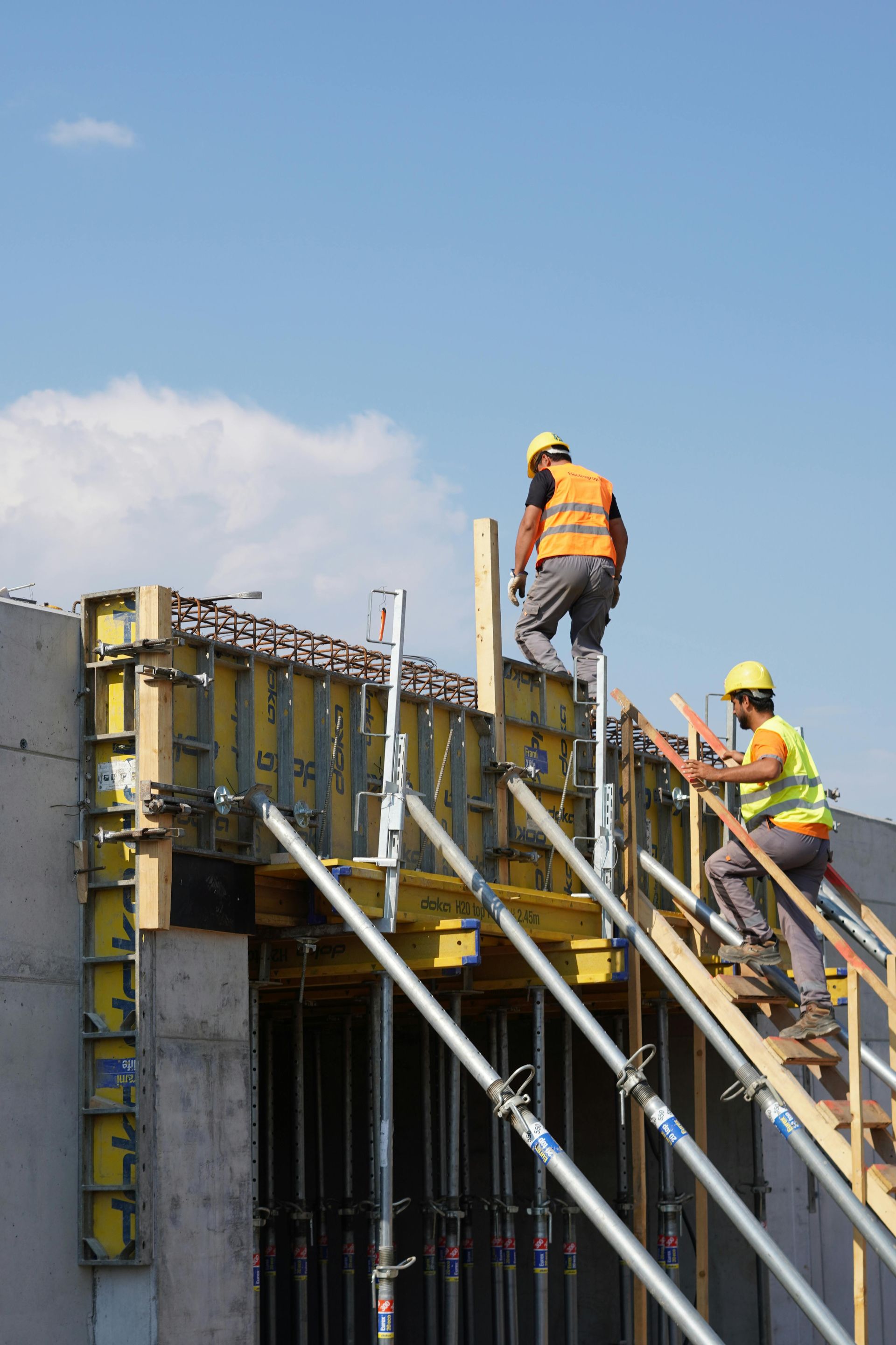 Deux ouvriers du bâtiment, casques de chantier sur la tête, travaillent sur un échafaudage.