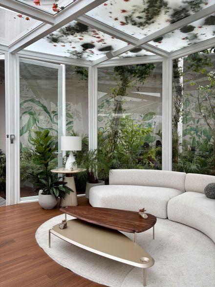Véranda moderne avec canapé d'angle blanc, table basse en bois, plantes et plafond en verre