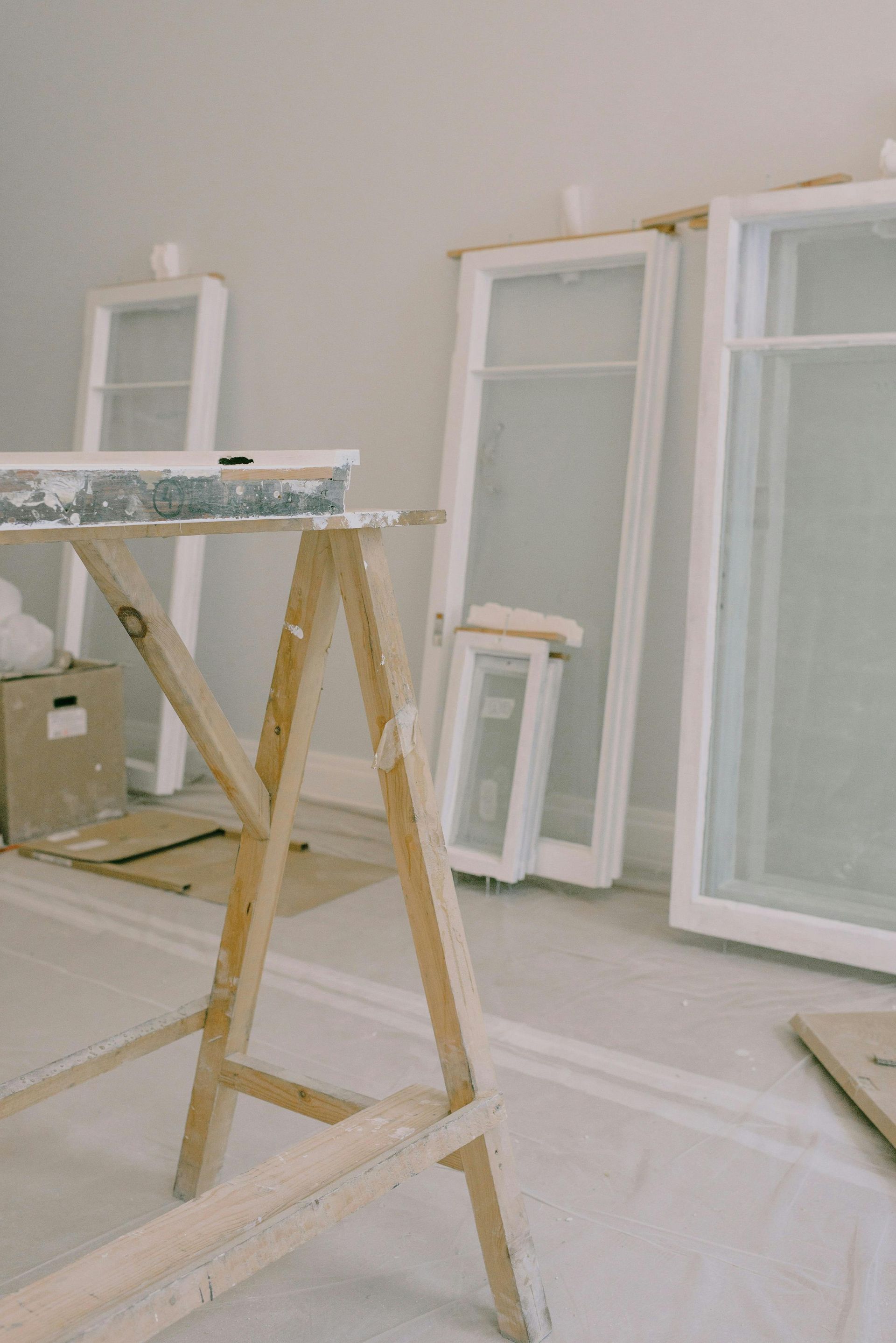Pièce en rénovation avec tréteaux, cadres de fenêtres blancs inclinés et matériaux de construction au sol