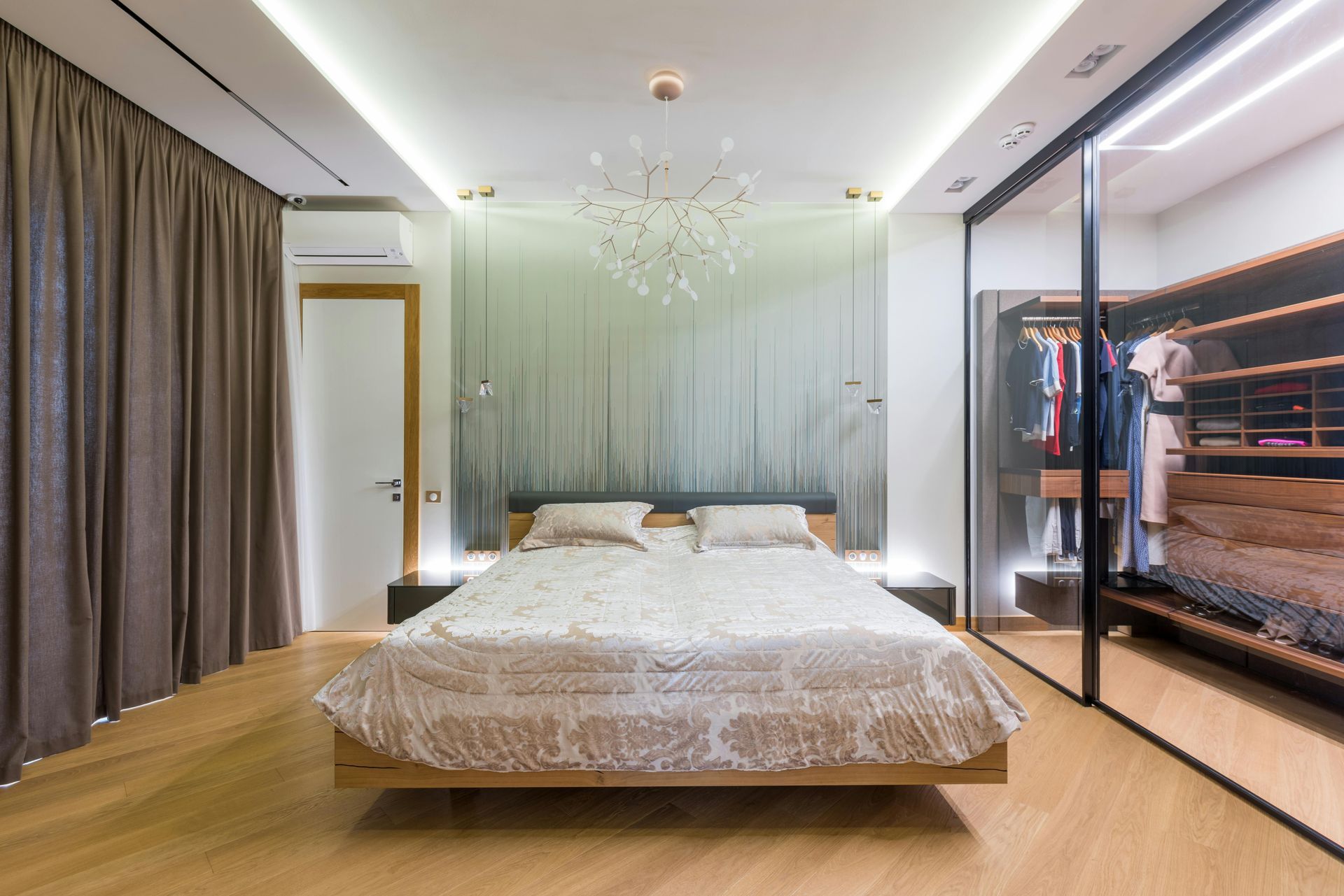 Chambre moderne avec lit, paroi en verre dépoli, lustre et placard à miroir dans des tons neutres chauds.