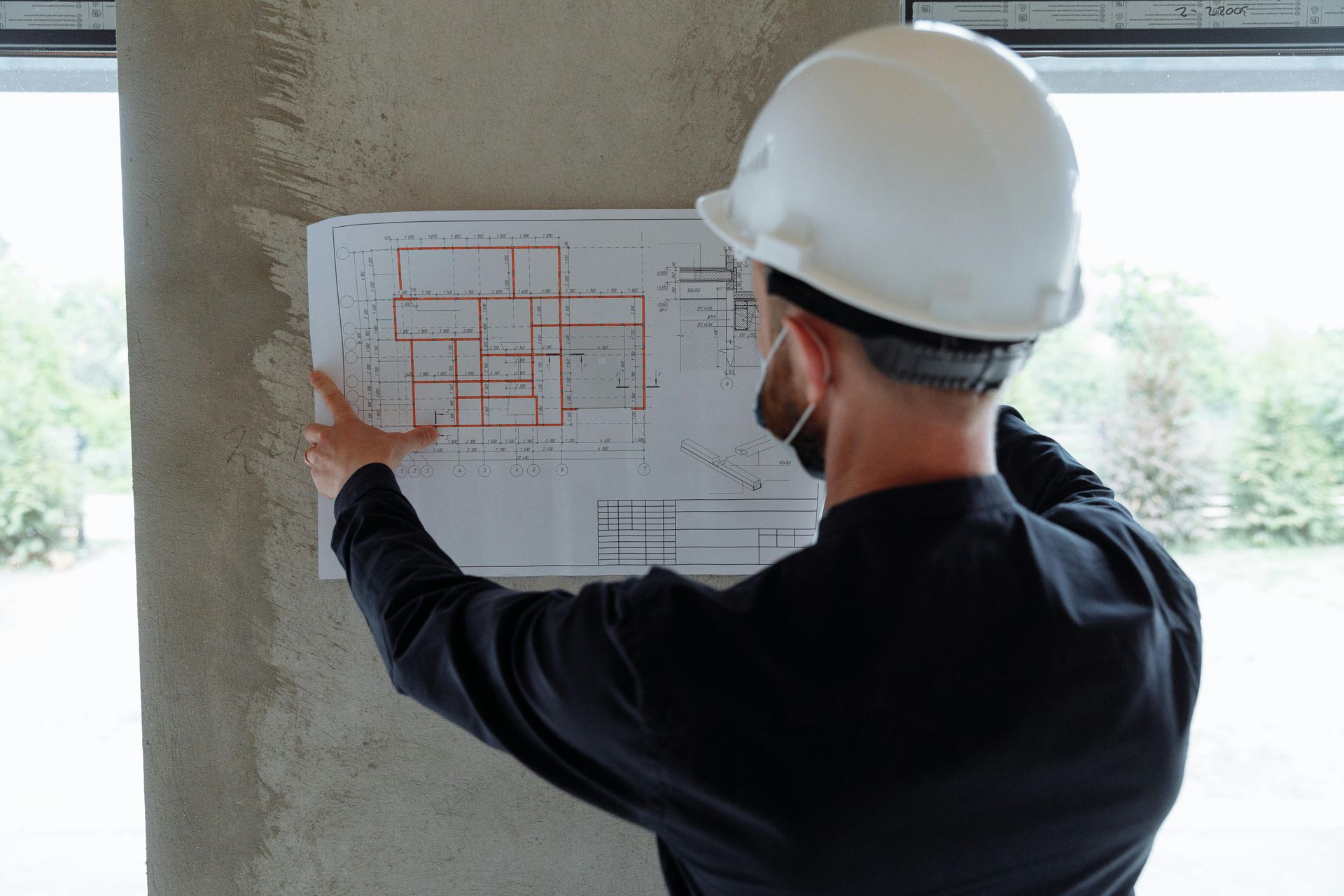 Un ouvrier du bâtiment, portant un casque blanc, examine des plans sur un mur en béton.