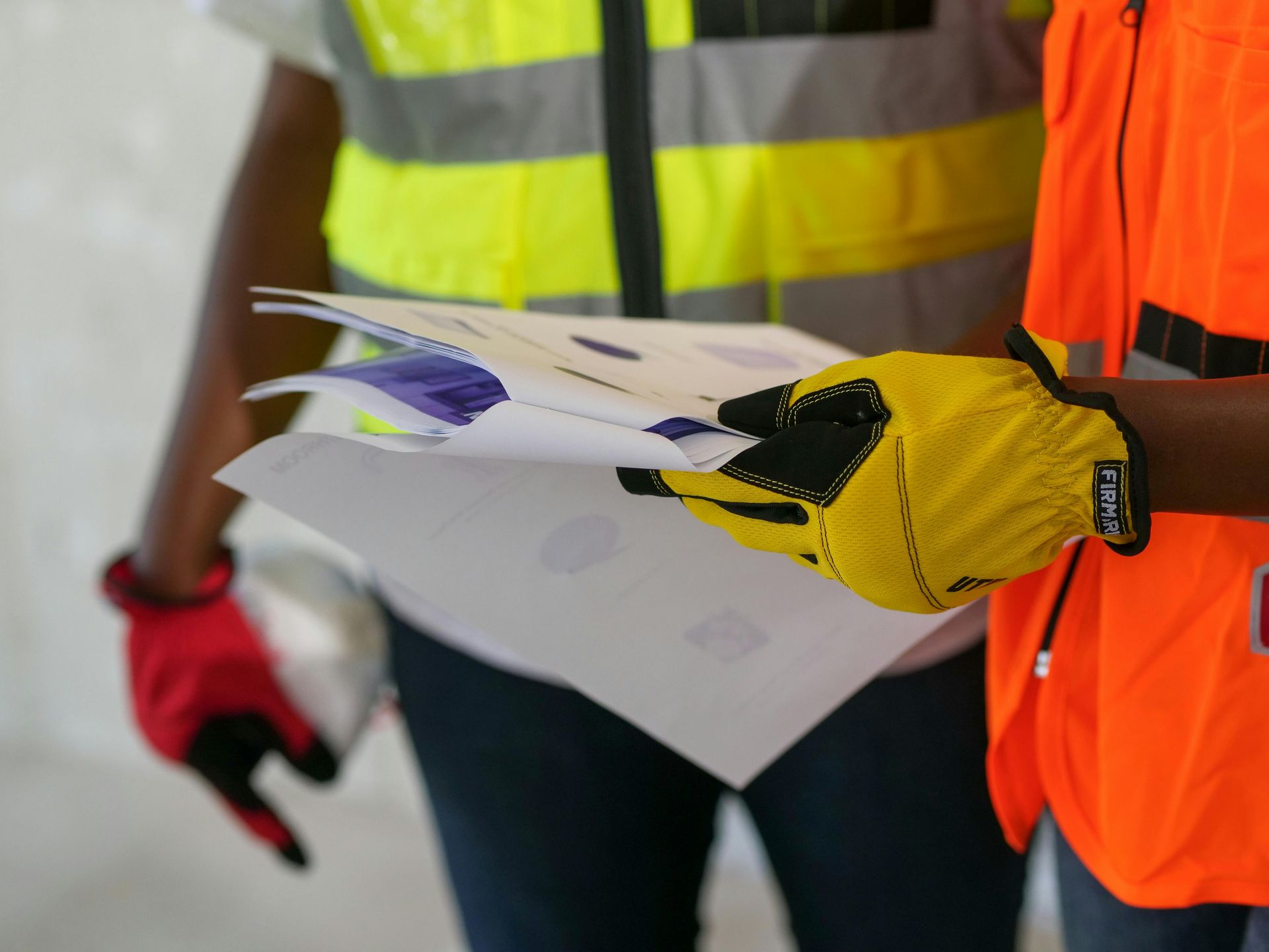 Des ouvriers portant des gilets de sécurité tiennent et examinent des plans papier à l'extérieur