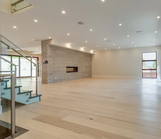 Salon moderne et spacieux avec parquet clair, cheminée en pierre, escalier en verre et éclairage encastré