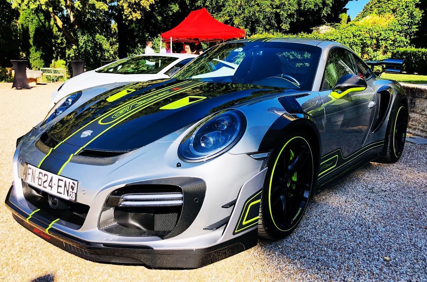 Voiture de sport Porsche argentée avec des accents noirs et vert fluo, garée à l'extérieur.