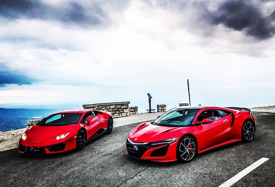 Des voitures de sport Lamborghini rouges et Honda NSX sur une route de montagne sous un ciel nuageux.