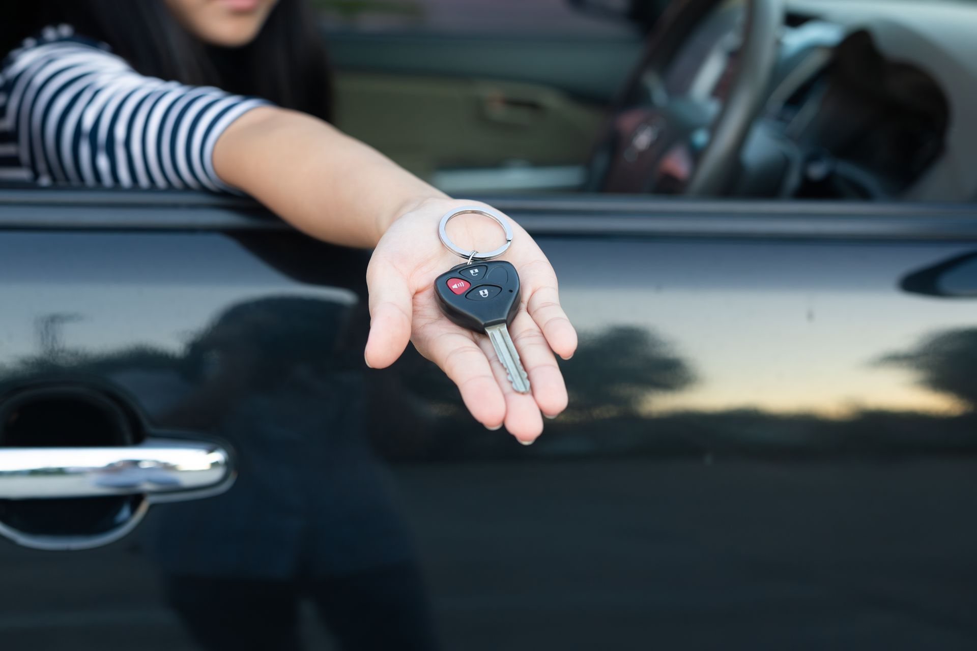 Personne tendant ses clés de voiture, la main à l'extérieur de la fenêtre de la voiture.