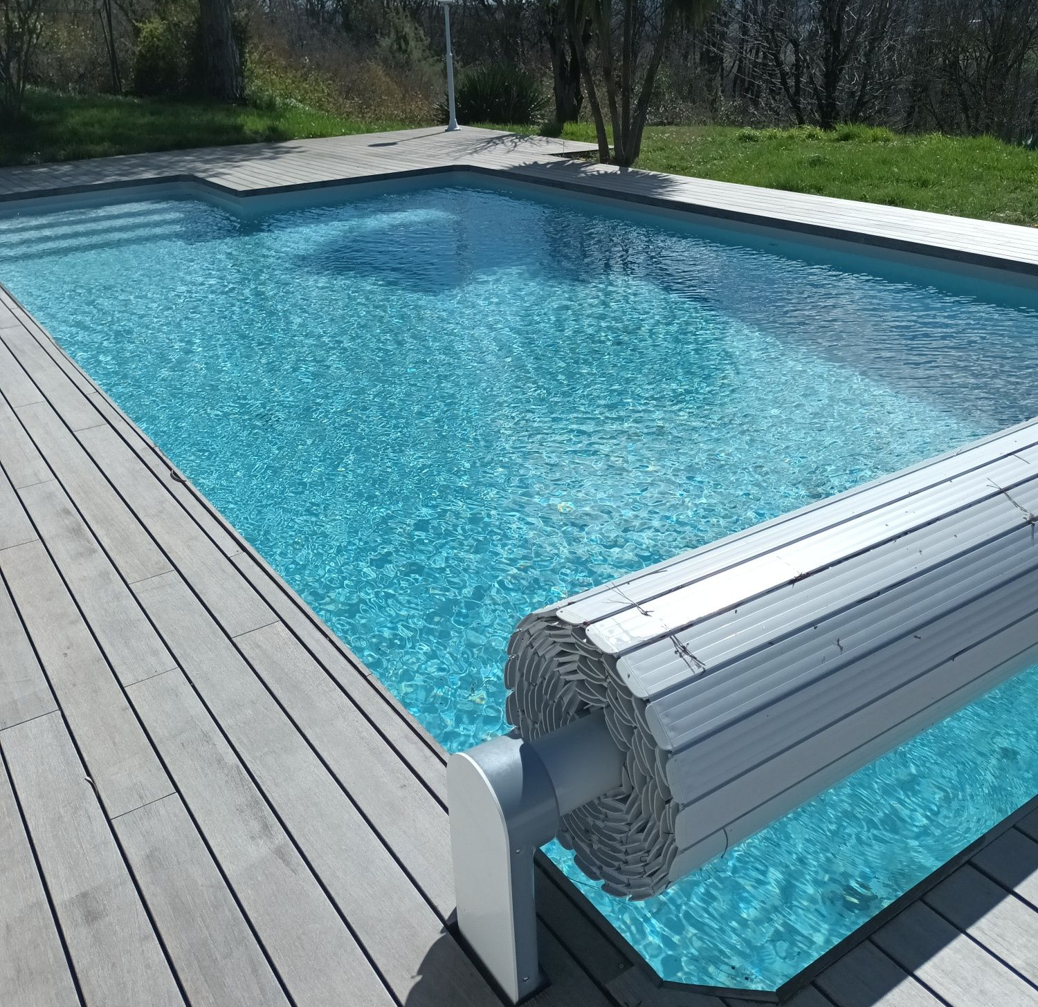 Piscine avec eau bleue et couverture enroulable partiellement couverte entourée d'une terrasse en bois.