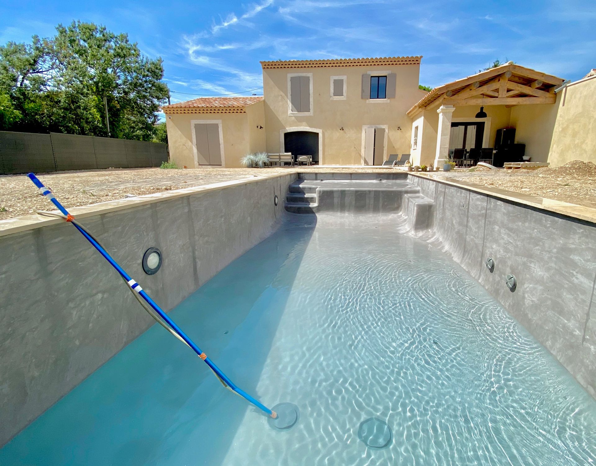 Un homme et une femme souriants, tenant une brochure devant le bâtiment TEC PISCINES. Journée ensoleillée.