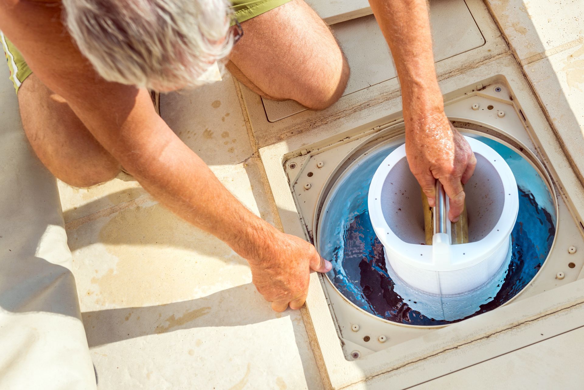Personne nettoyant un skimmer de piscine, retirant un filtre blanc.
