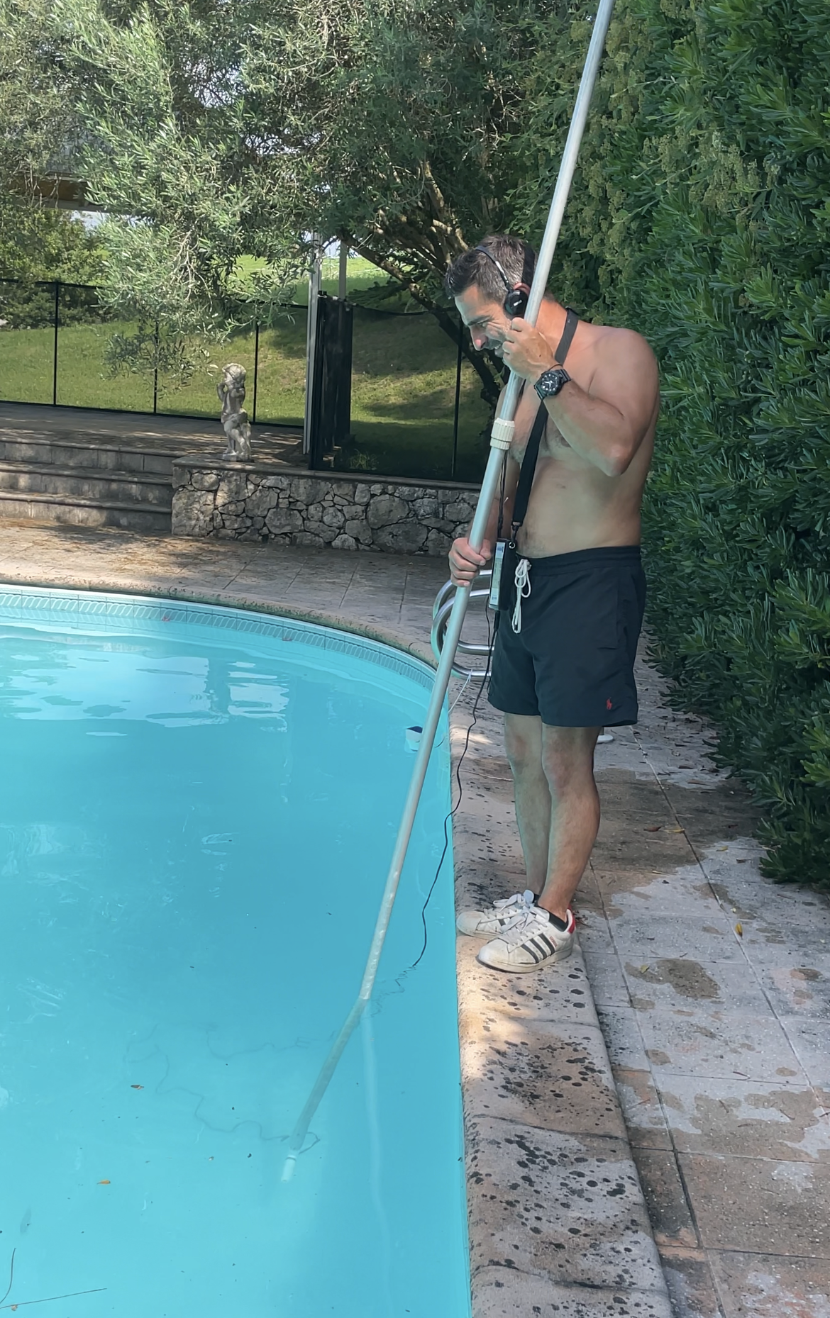 Personne nettoyant une piscine turquoise avec un filet attaché à un poteau, debout sur une terrasse en bois.