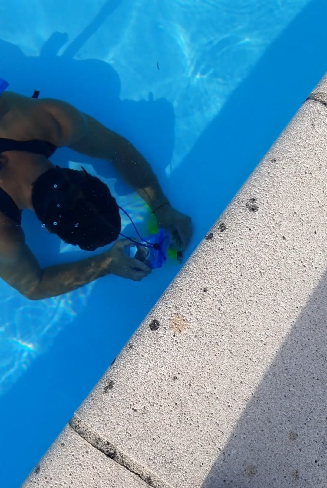 Main d'homme immergée dans l'eau bleue d'une piscine, pressant une éponge blanche, avec un fond clair.