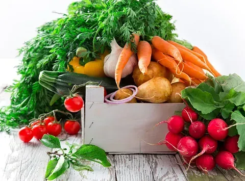 Verduras frescas, incluidas zanahorias, rábanos, tomates y eneldo, derramándose de una caja de madera.