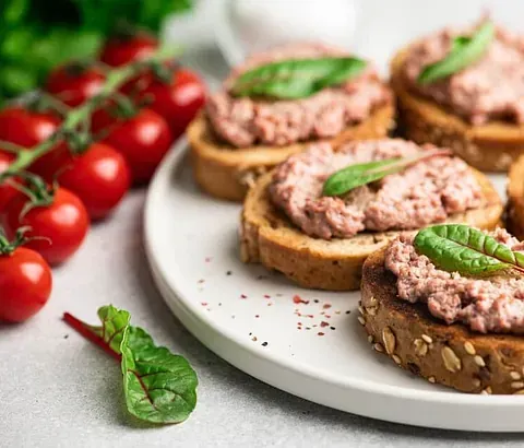 Rebanadas de pan tostado con paté cubierto con albahaca, servido con tomates cherry.