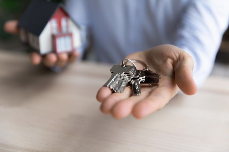 Eine Person hält einen Schlüsselbund und ein kleines Haus in der Hand.