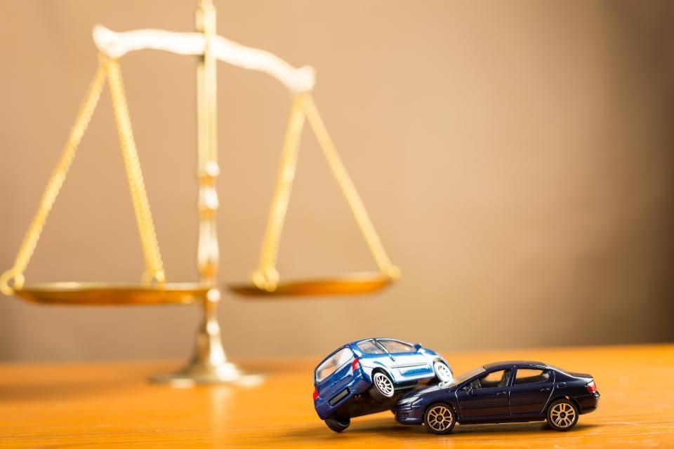 Zwei Spielzeugautos stehen auf einem Holztisch vor einer Waage der Gerechtigkeit.