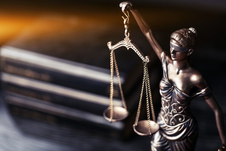 Eine Statue der Justitia, die vor einem Buch eine Waage hält.