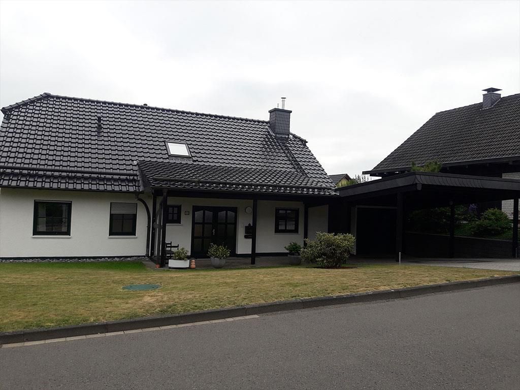 Ein weißes Haus mit schwarzem Dach und einem Carport davor.