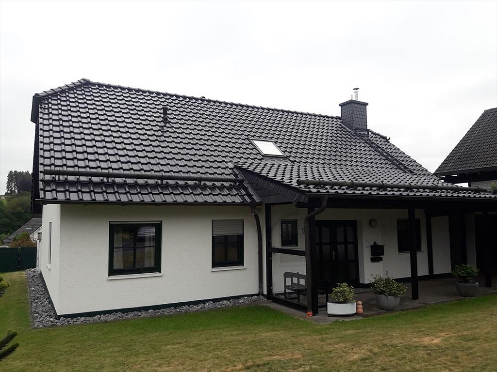 Ein weißes Haus mit schwarzem Dach und einer Bank davor.