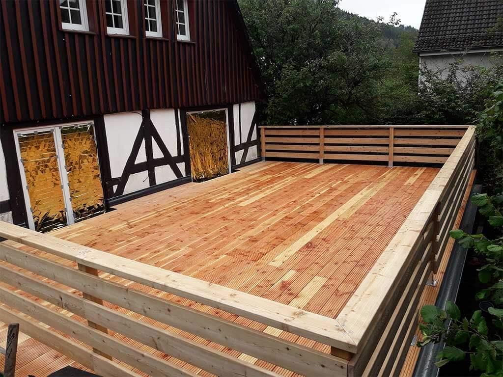 Vor einem Haus befindet sich eine Holzterrasse mit Zaun.