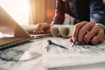 Person arbeitet mit Laptop und Bauplänen