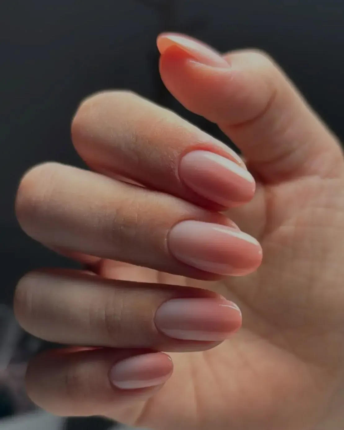 Primer plano de una mano con uñas cortas y de color rosa pálido.