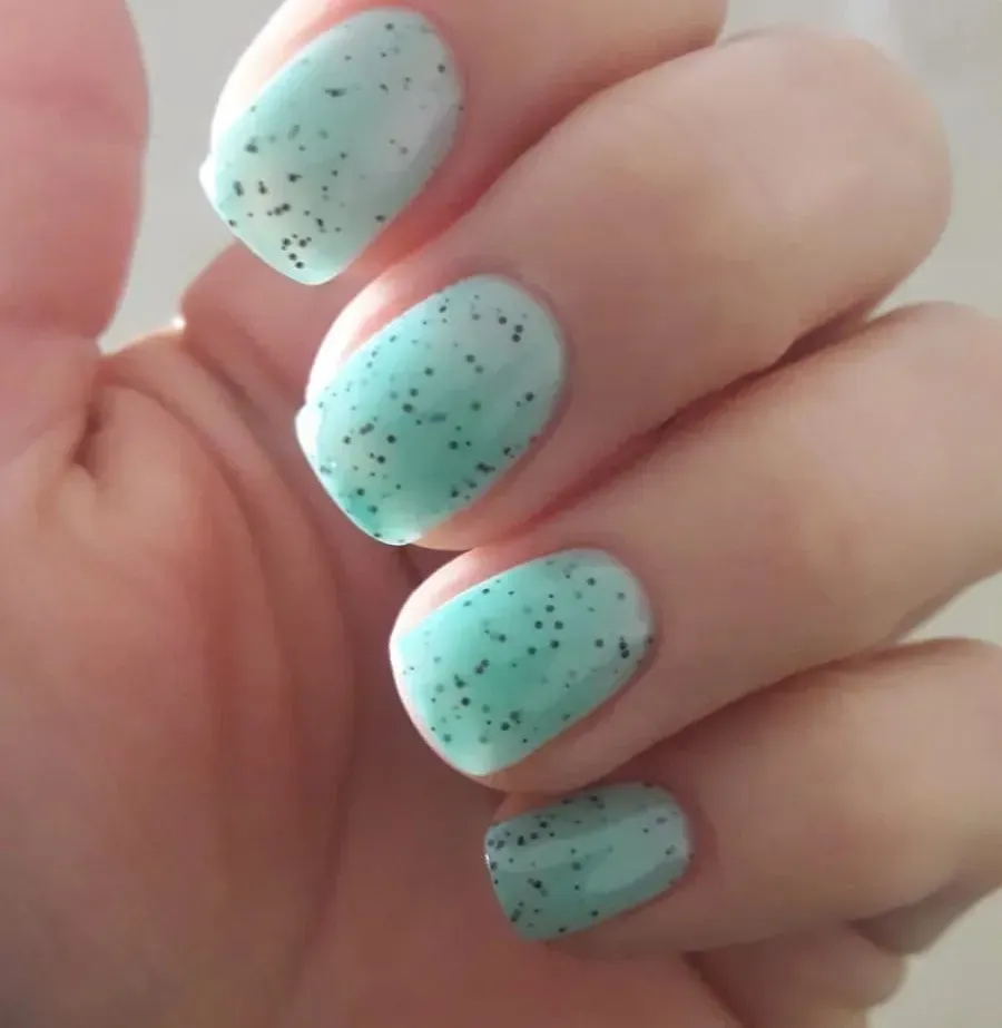 Primer plano de uñas verde menta con motas negras en una mano.
