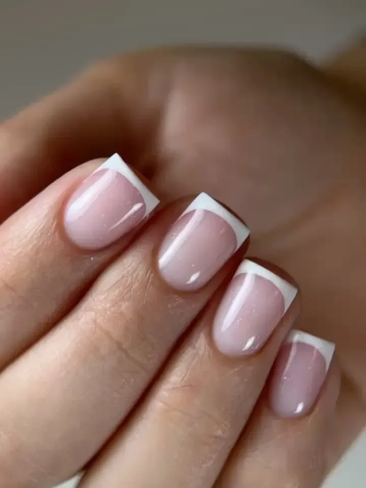 Primer plano de manos con uñas pintadas de rosa pálido brillante con manicura francesa.