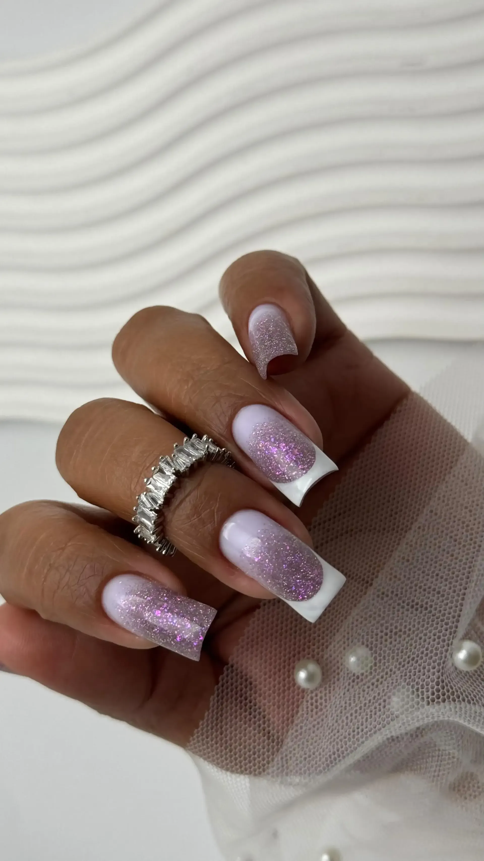 Mano con uñas largas de color rosa y blanco con punta francesa, que lleva un guante de malla transparente.