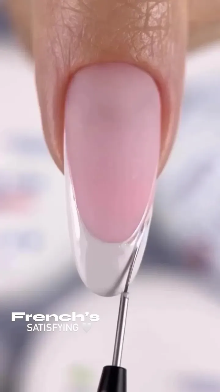 Primer plano de un dedo con la uña pintada de color rosa pálido y la punta pintada con una manicura francesa blanca.