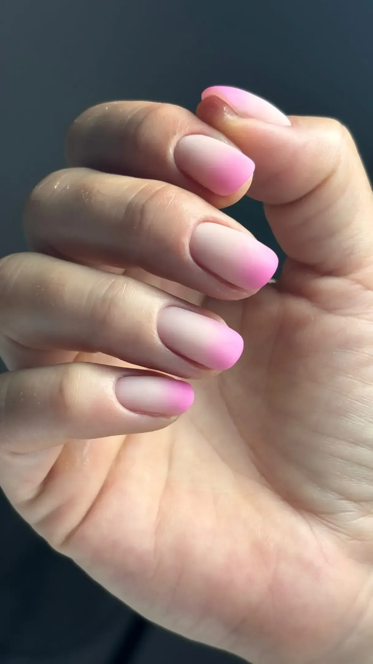 Primer plano de una mano con uñas pintadas en degradado rosa, cerradas en un puño.