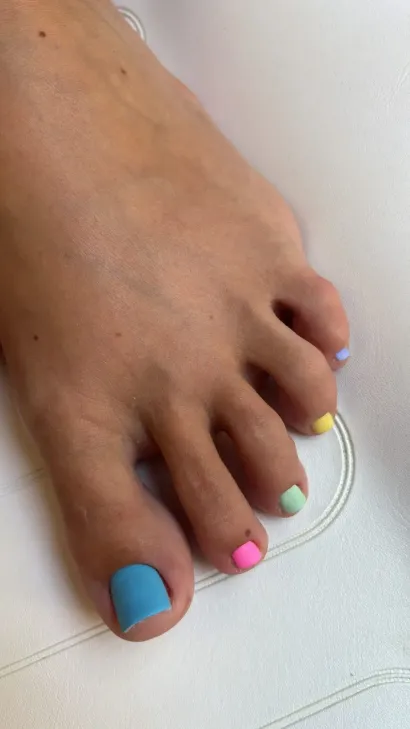 Pies descalzos con pedicura rosa pálido junto a una vela encendida y una suave decoración de spa.