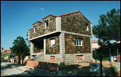 Casa de piedra con base de ladrillo rojo y ventanas con marcos blancos bajo un cielo azul.