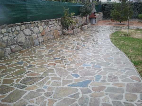 Sendero ajardinado empedrado que serpentea junto a un muro de piedra y un borde de césped.