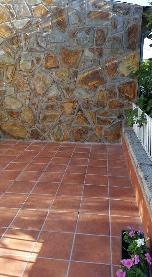 Patio con suelo de terracota junto a un muro de piedra, con una pequeña jardinera en la esquina.