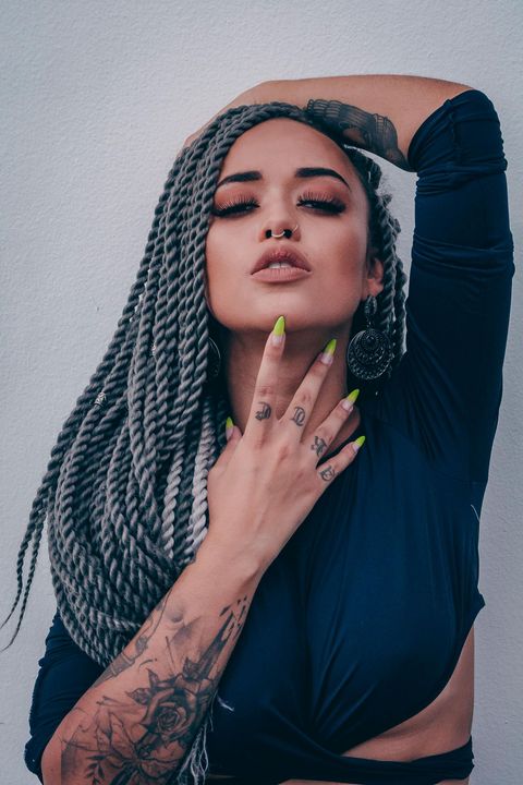 Una mujer con trenzas y un tatuaje en el brazo posa para una fotografía.