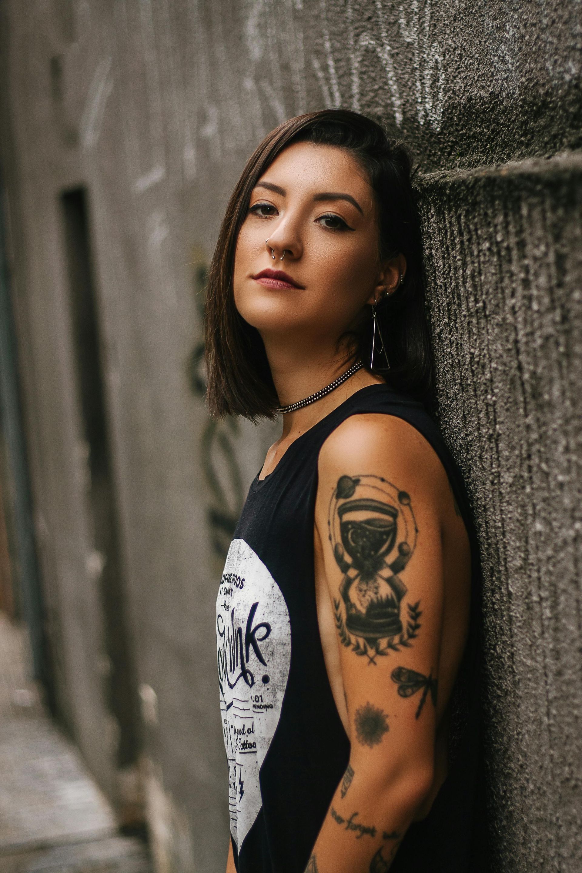 Una mujer con muchos tatuajes en el brazo está apoyada contra una pared.