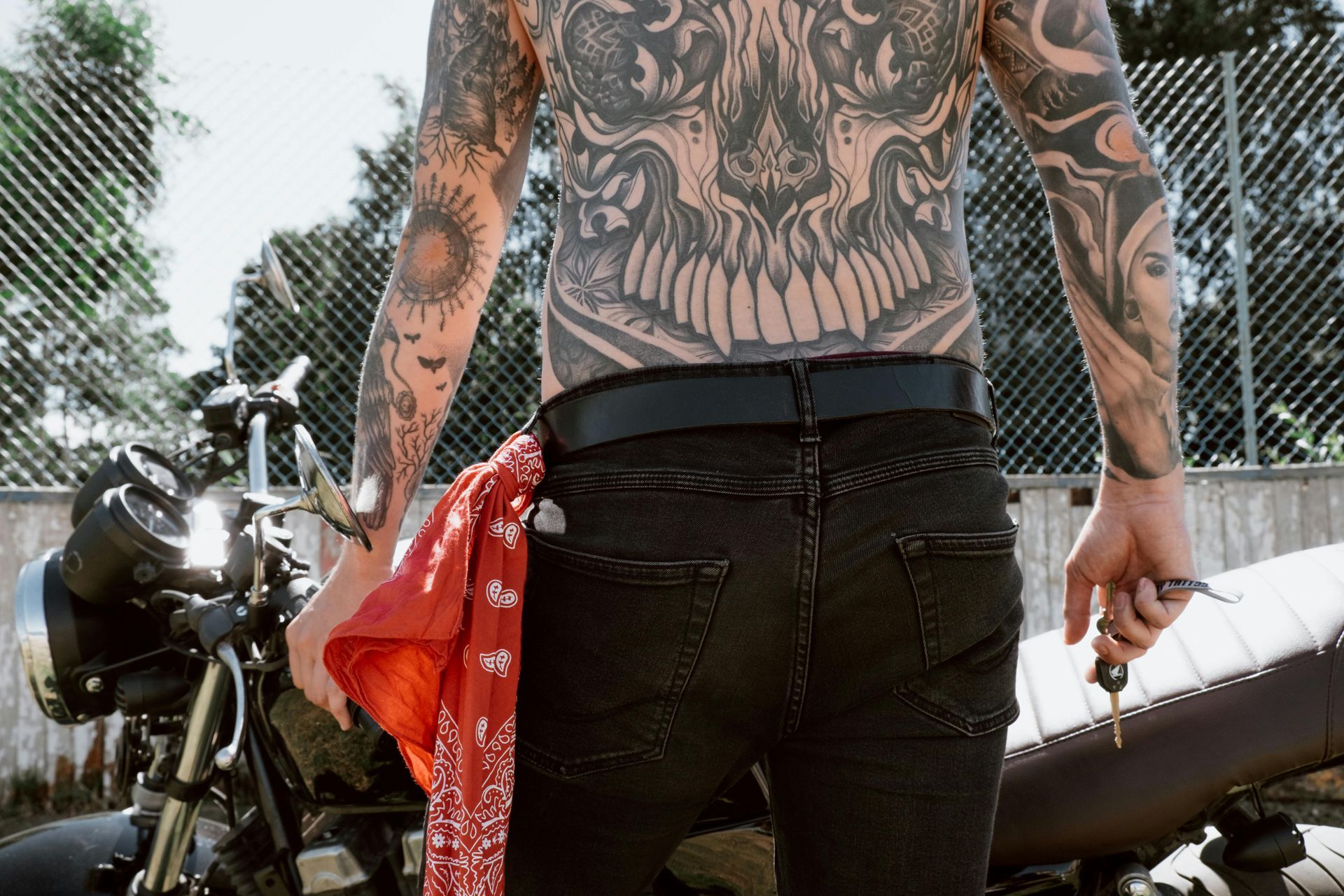Un hombre con un tatuaje en la espalda está de pie junto a una motocicleta.