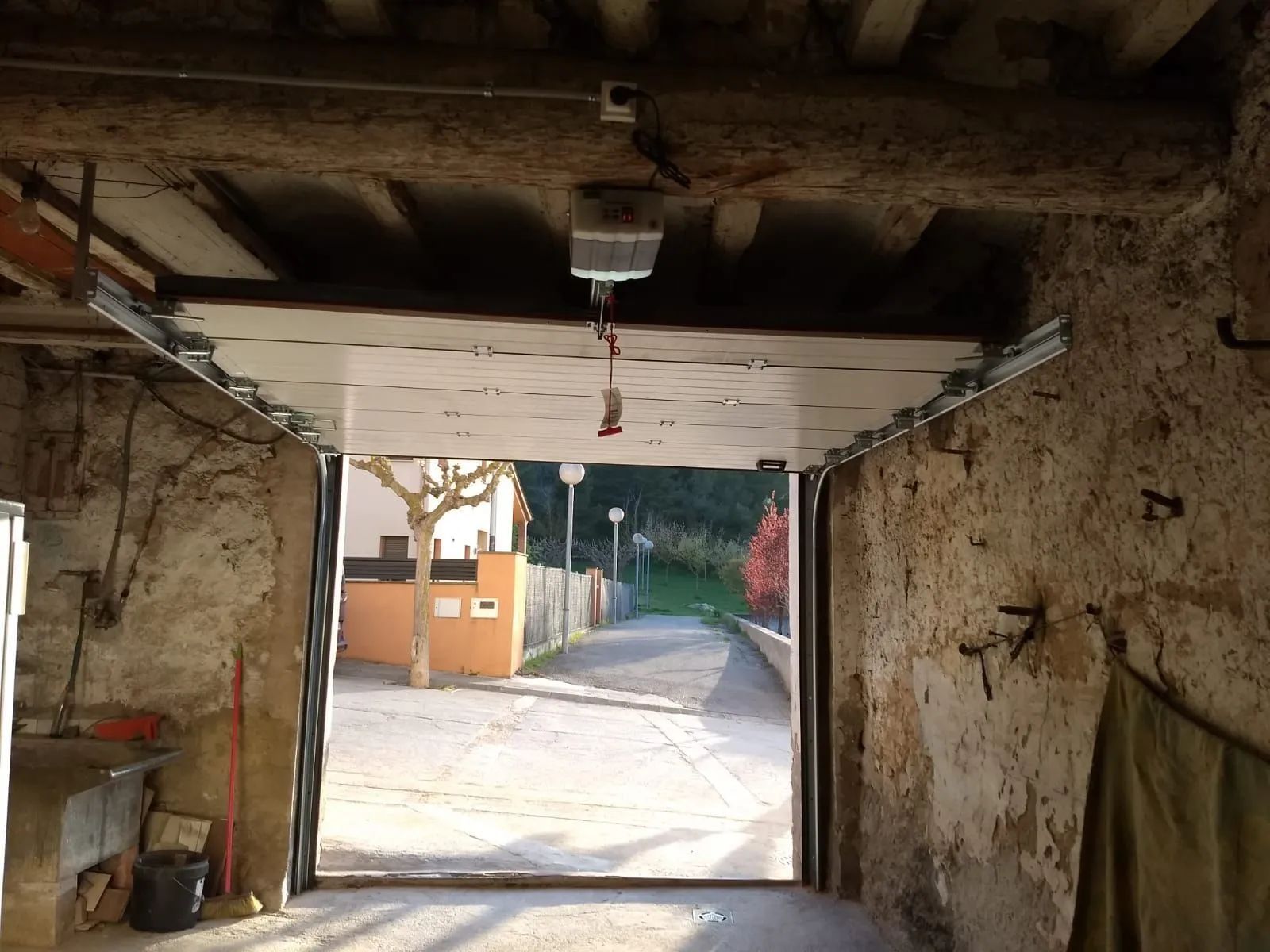 Puerta de garaje abierta con puerta superior blanca y vista a una calle, árboles y edificios.