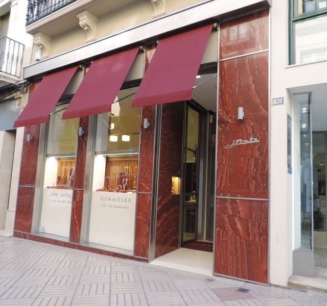 Exterior de joyería con toldos rojos, paredes de mármol y escaparates.