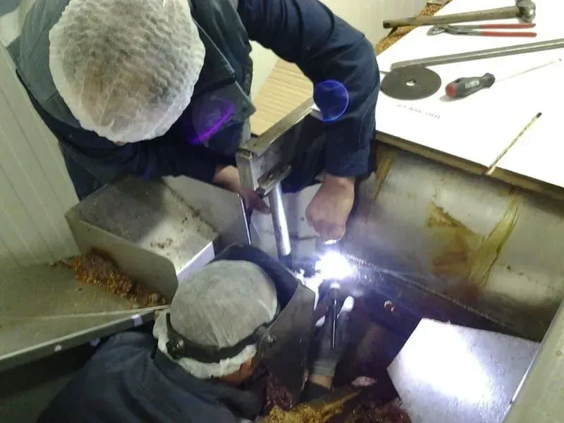 Dos personas soldando dentro de una máquina procesadora de alimentos de metal.