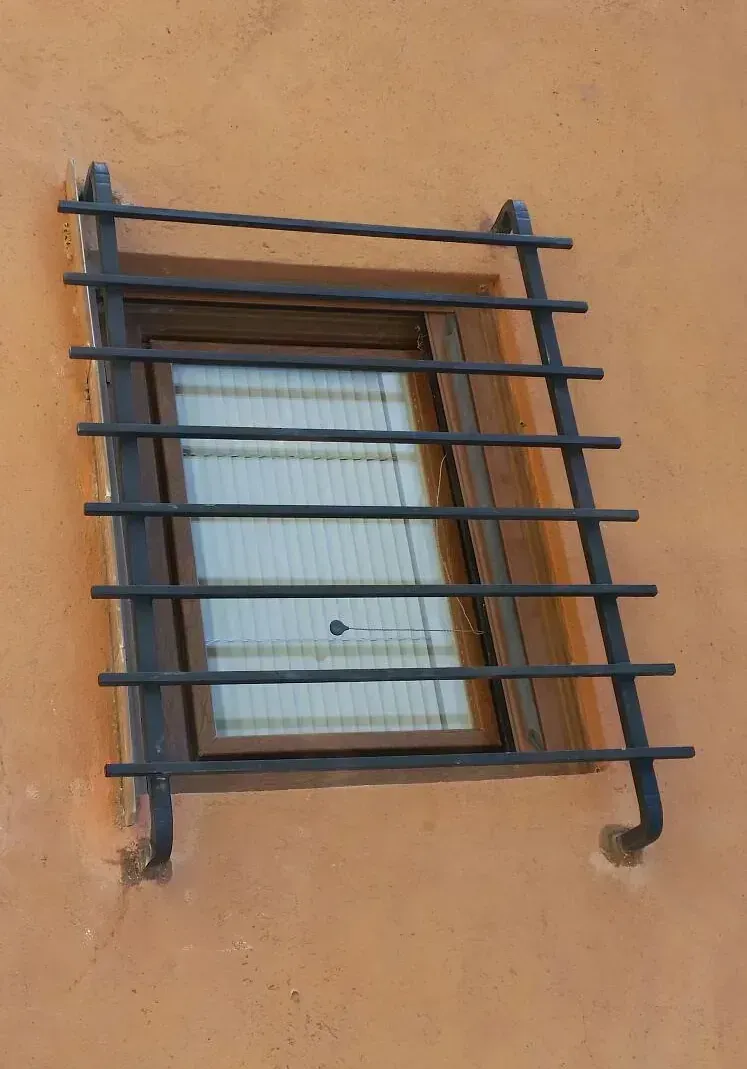 Ventana con rejas de seguridad de metal negro sobre pared naranja.