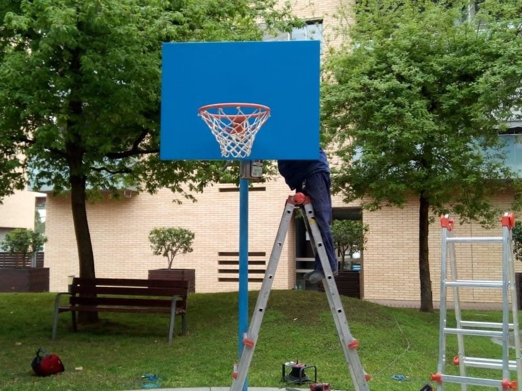 Persona en una escalera instalando un aro de baloncesto azul en un parque.