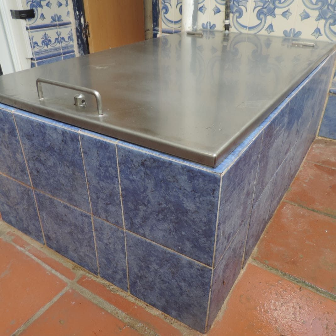 Enfriador con cubierta de acero inoxidable y base de azulejos azules sobre un patio de ladrillo.