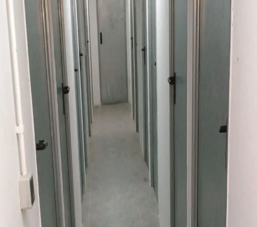 Pasillo estrecho con muchas puertas grises idénticas a ambos lados.