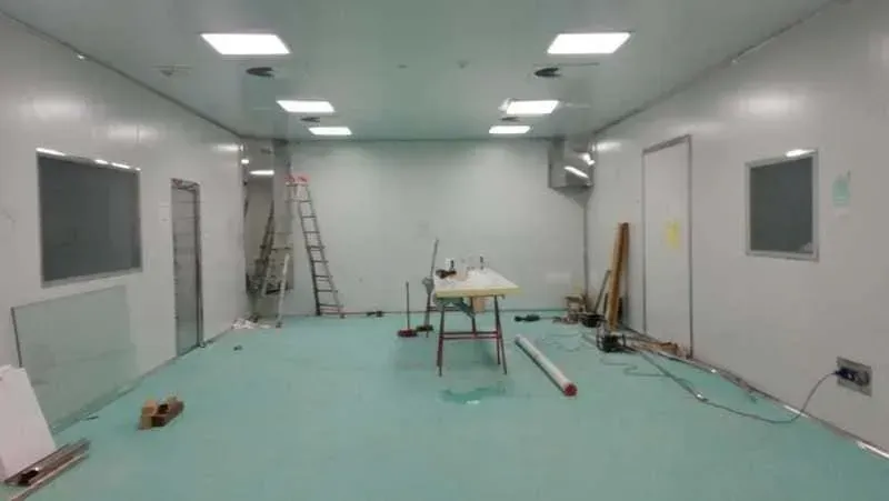 Una sala limpia con paredes blancas y piso verde azulado, que contiene una escalera, una mesa y varios equipos.